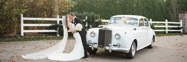 A wide shot of a bride and groom kissing in front of a vintage car in Utah
