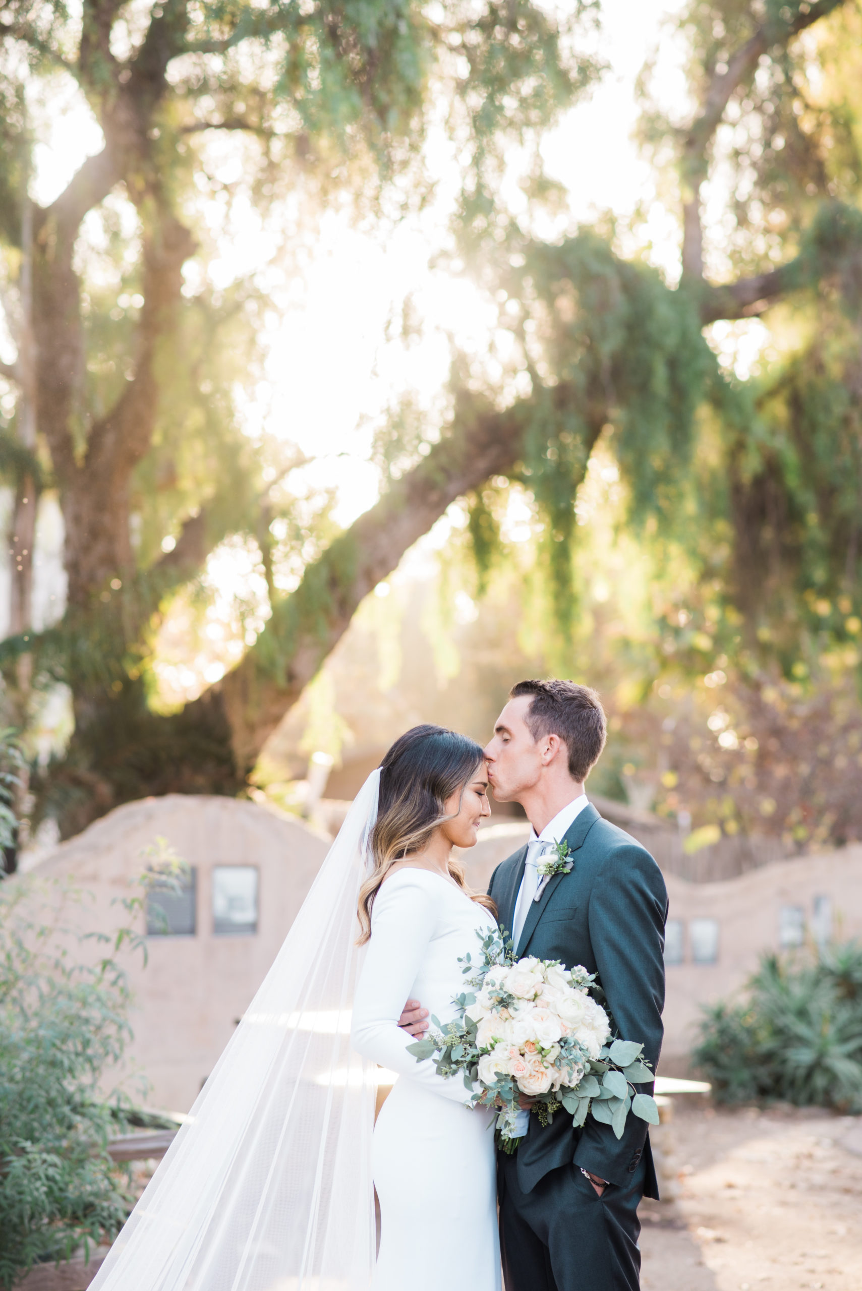 Groom kisses bride's forehead in their garden wedding venue in Orange County, CA.