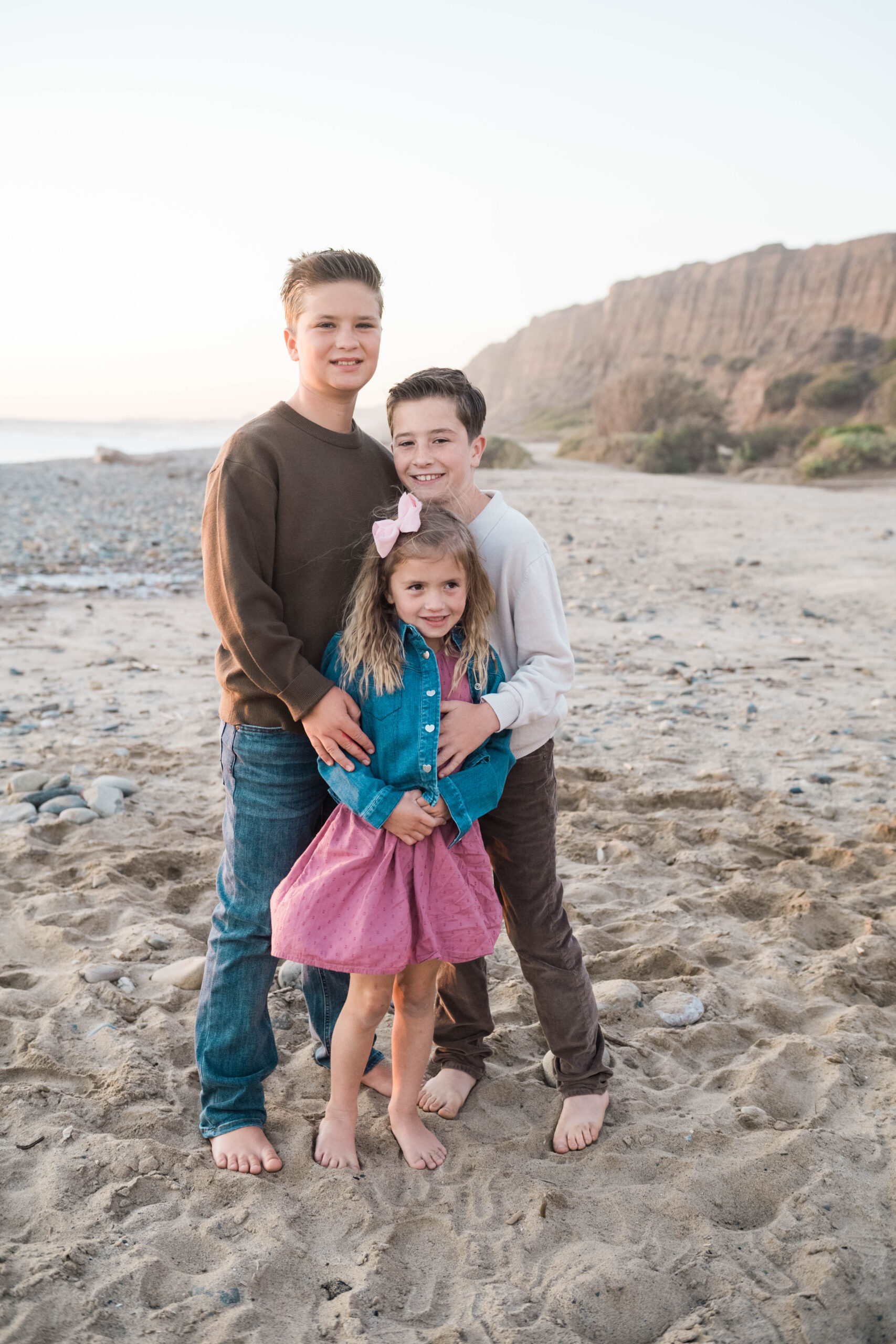 Siblings hugging on the beach during golden hour, Southern California family photography
