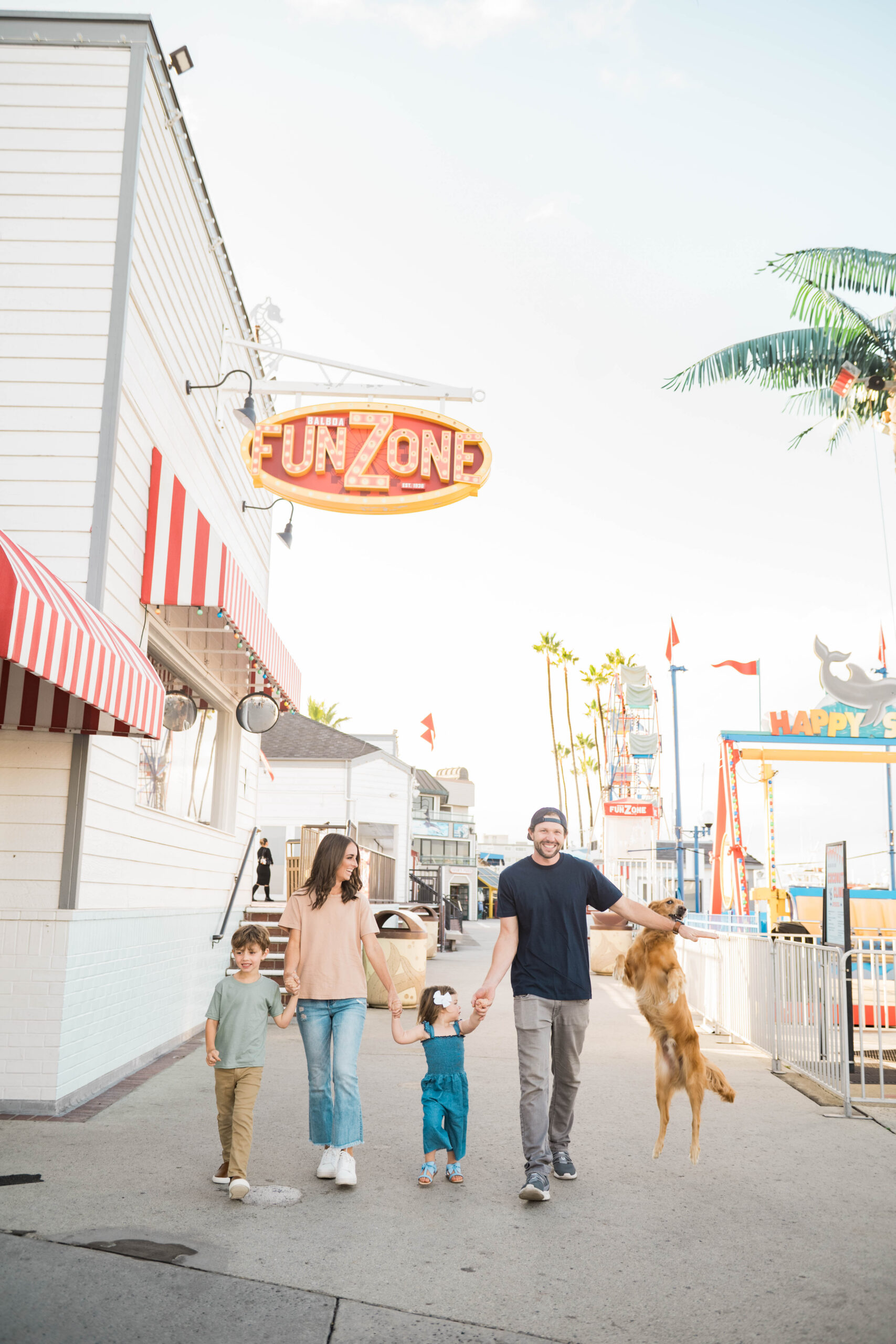 Family walking with playful golden retriever leaping beside them near the Balboa Fun Zone