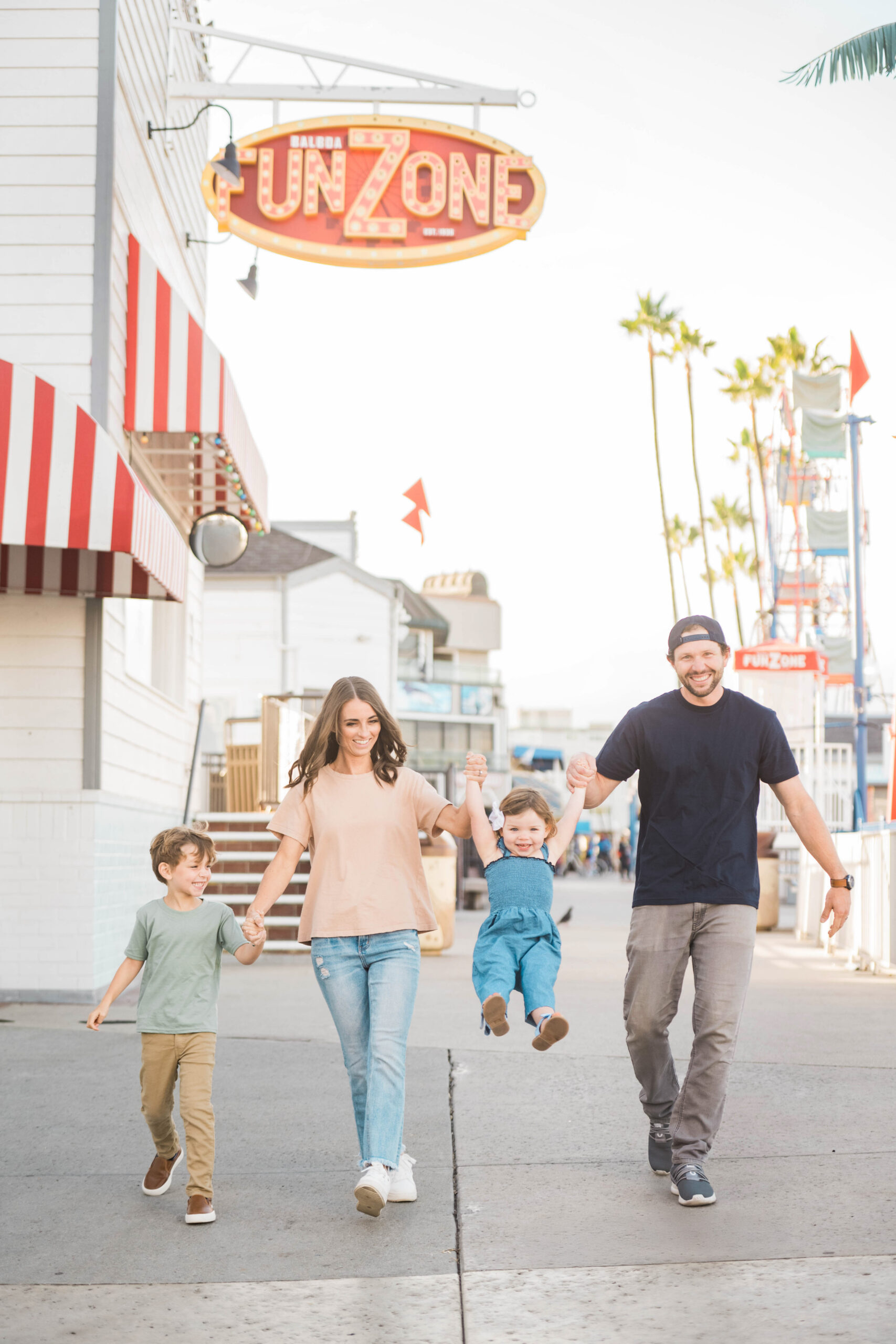 Family walking together with toddler swinging between them near the Balboa Fun Zone, Southern California