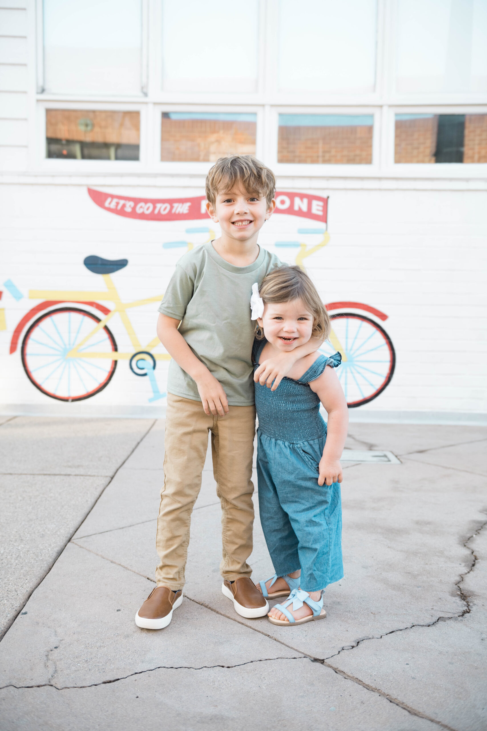 Brother and sister smiling together in front of a bike mural during family photos