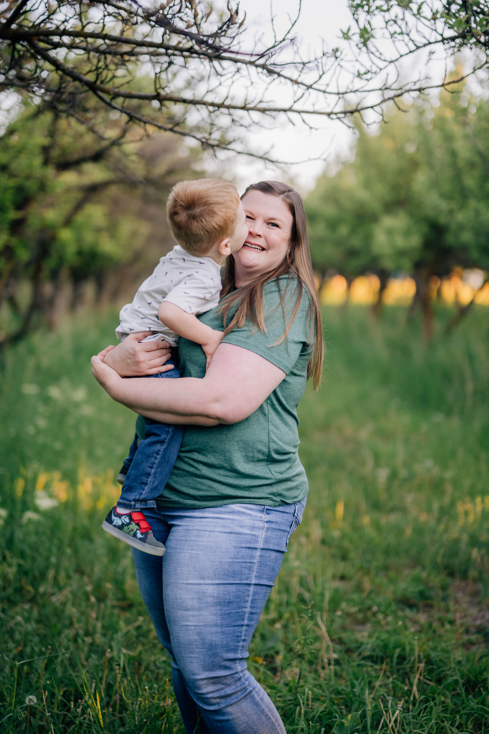Toddler kissing mom during summer family session in open field